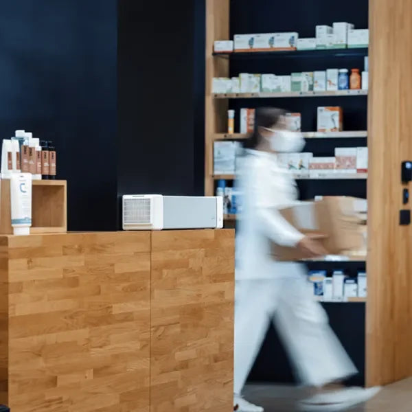 Purificador de aire germicida sobre mostrador de madera en farmacia, profesional con caja al fondo.