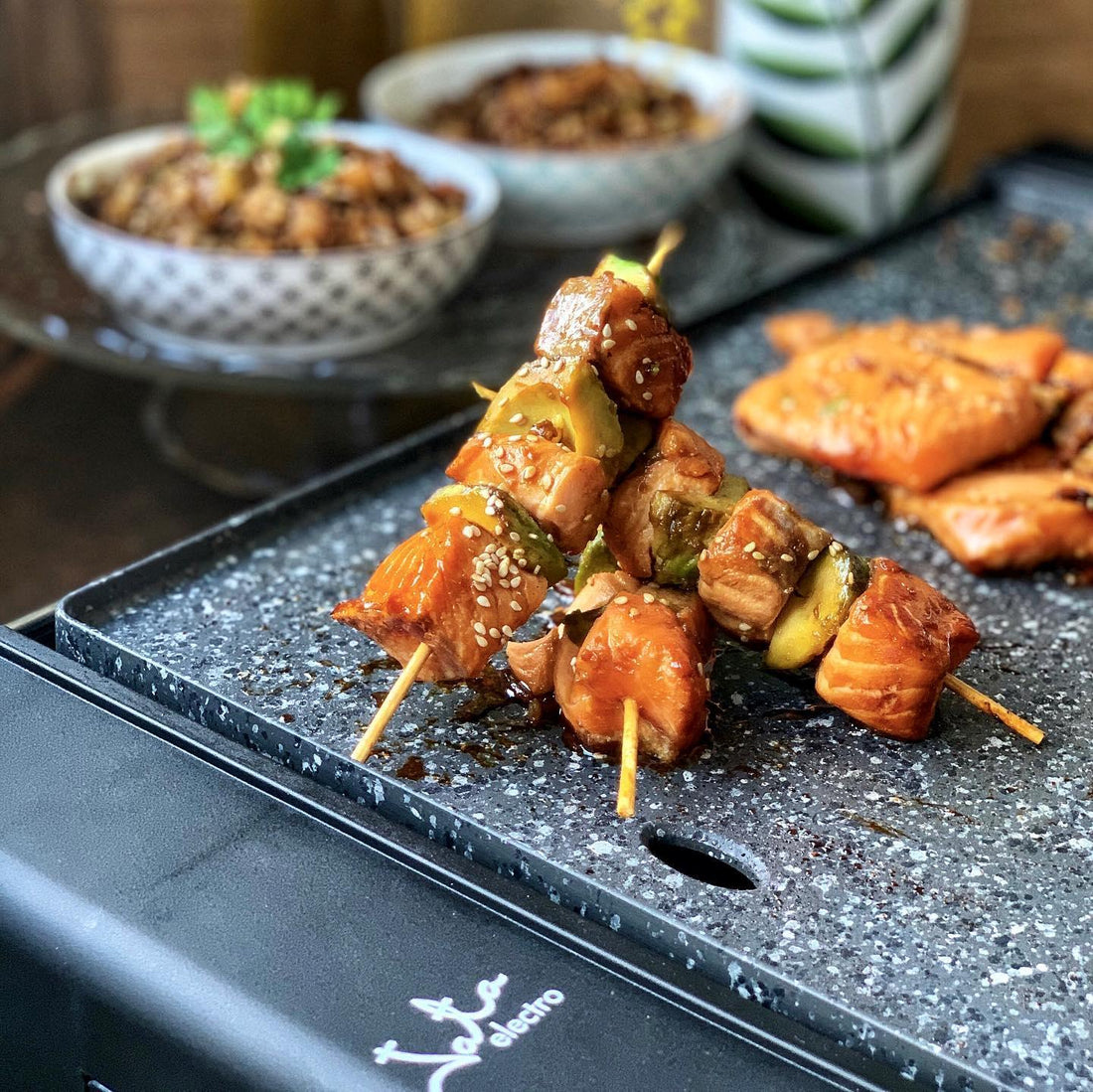 Brochetas de salmón y verduras cocinadas en parrilla eléctrica sobre mesa de cocina.