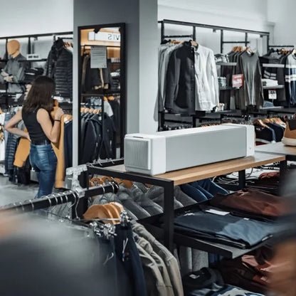 Purificador de aire rectangular sobre mesa en tienda de ropa moderna, prendas en exhibición